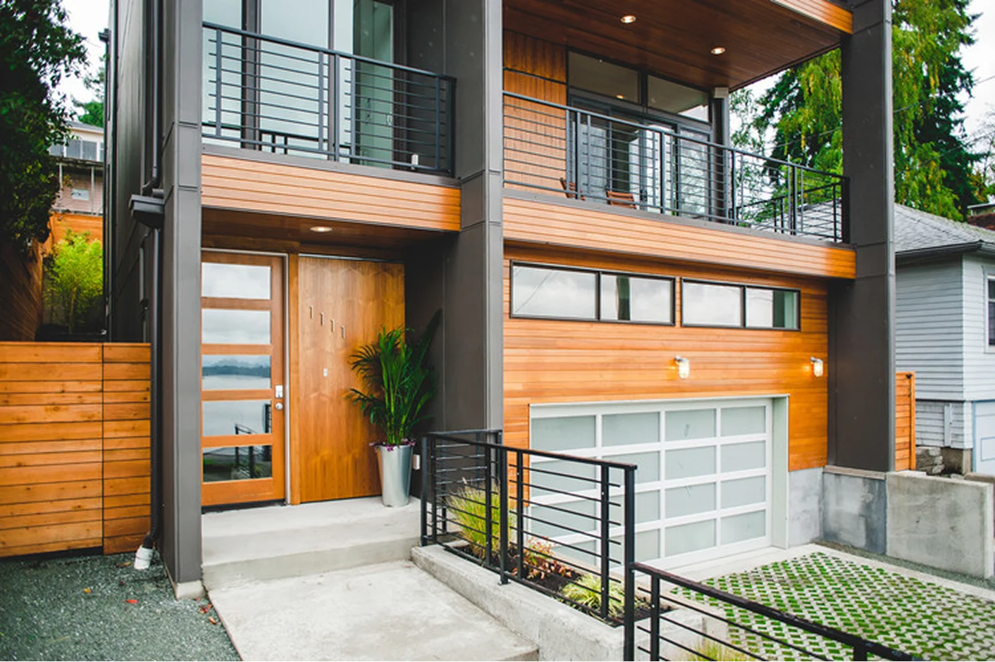 Custom metal solutions enhance this contemporary home entrance, featuring a wooden door with glass panels and a stylish metal railing.