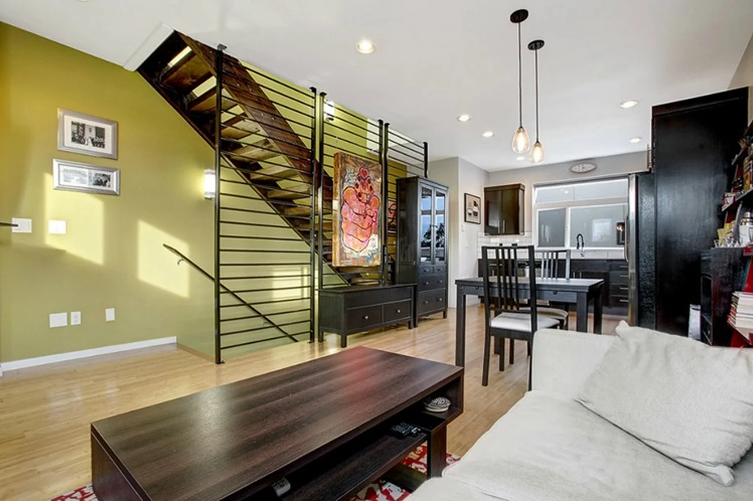 A modern living room with a stylish staircase, black railings, and wood steps, featuring minimalist furniture.