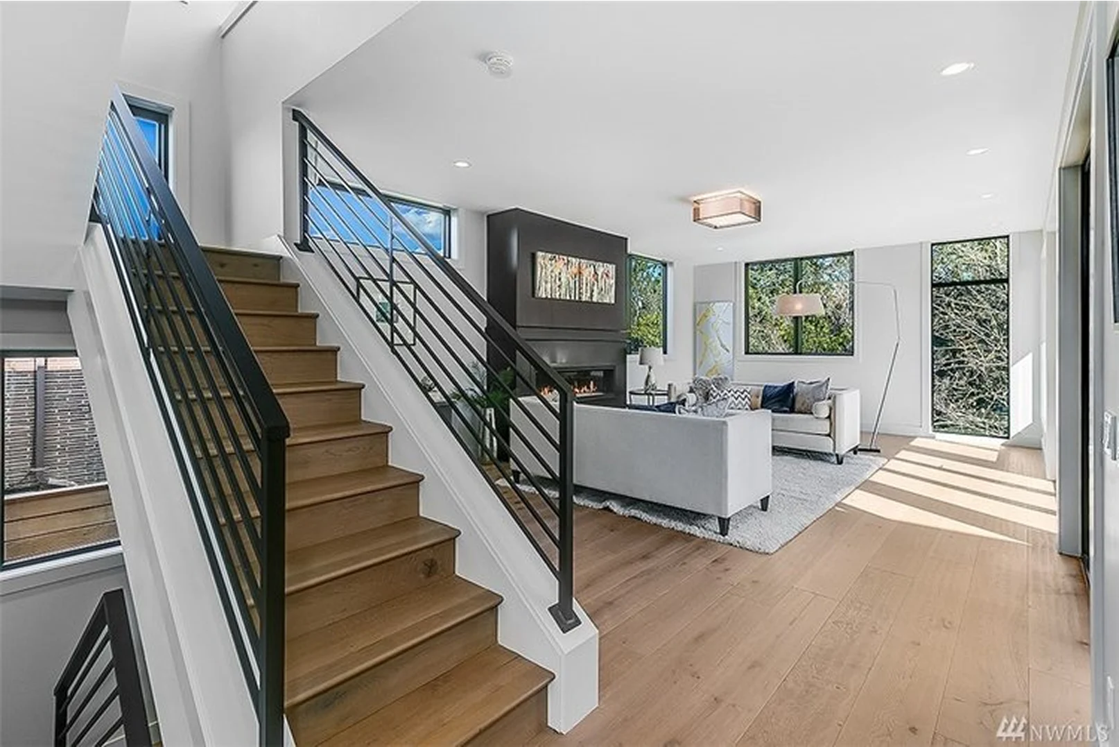 A stylish modern staircase leading to an open living room with large windows and contemporary furniture.